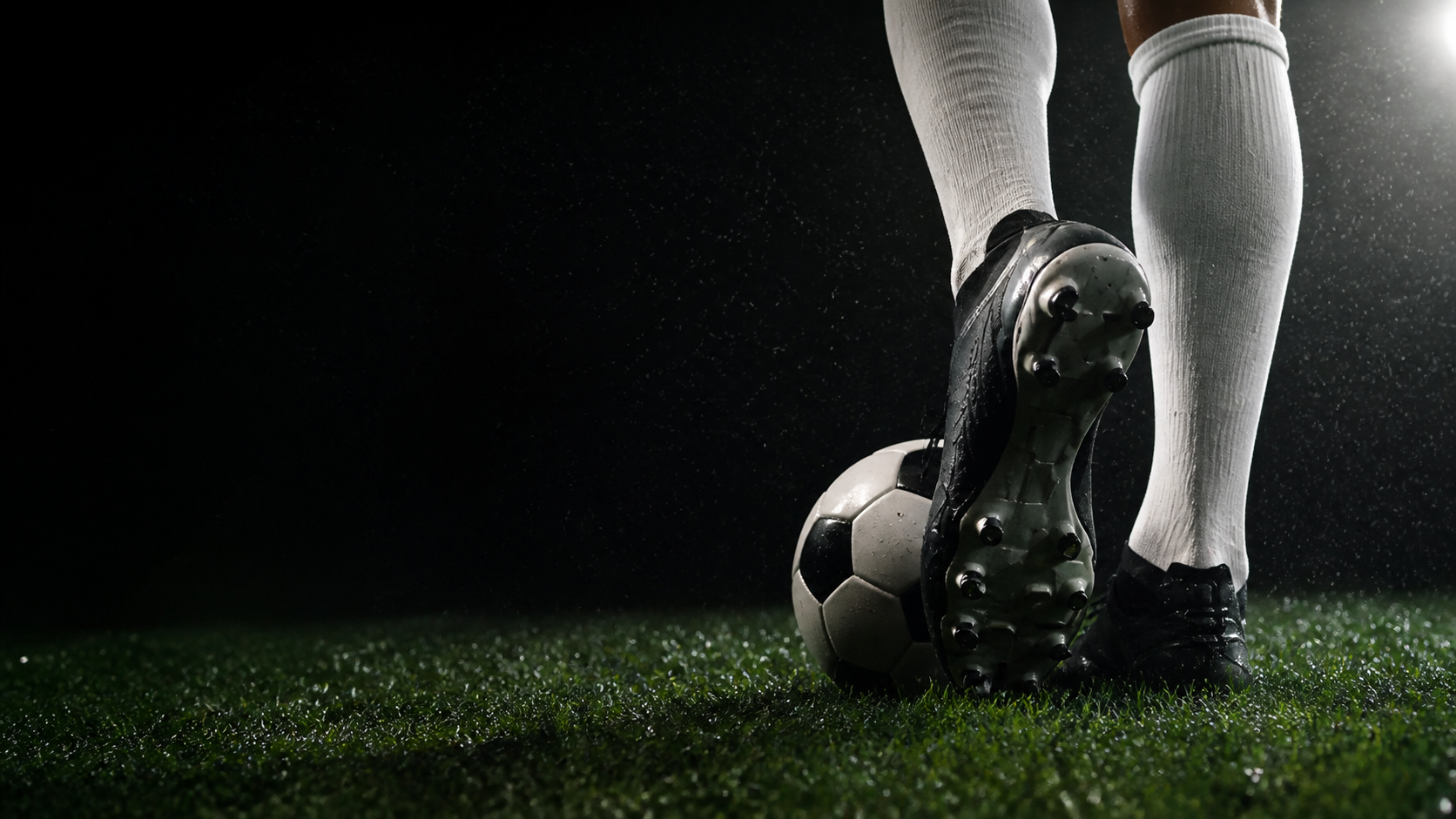 Chuteira de futebol junto à bola em um gramado molhado